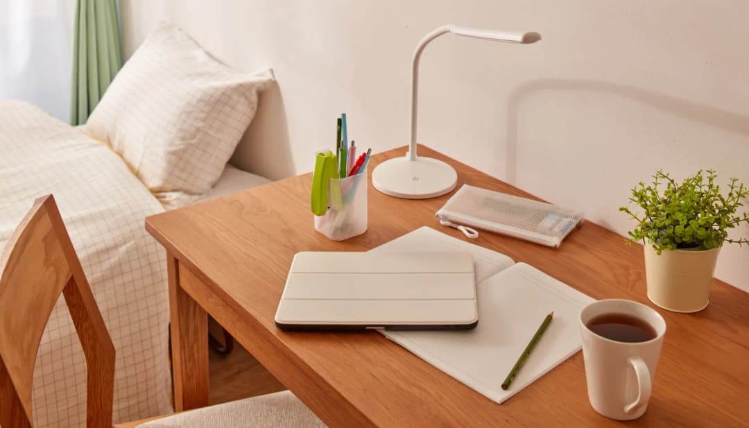 Kleiner Schreibtisch mit Tablet, Notizen und Kaffee neben einem Bett