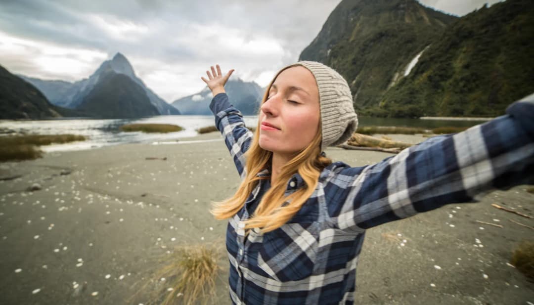 Frau breitet in einer Fjordlandschaft mit Bergen die Arme aus