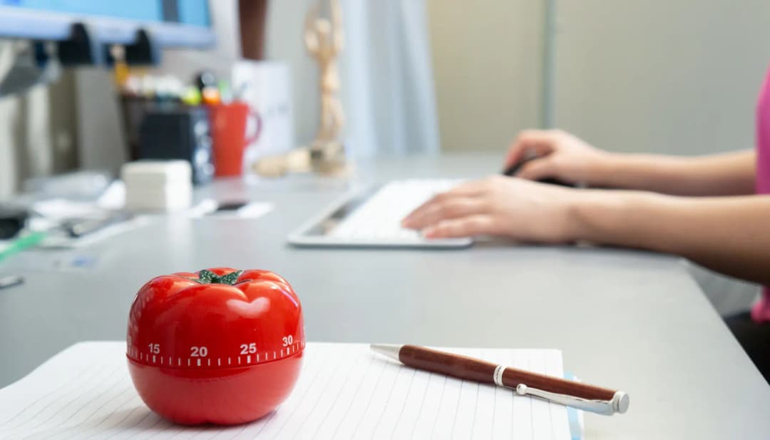 Tomaten-Küchenwecker auf dem Schreibtisch, im Hintergrund Hände an der Tastatur