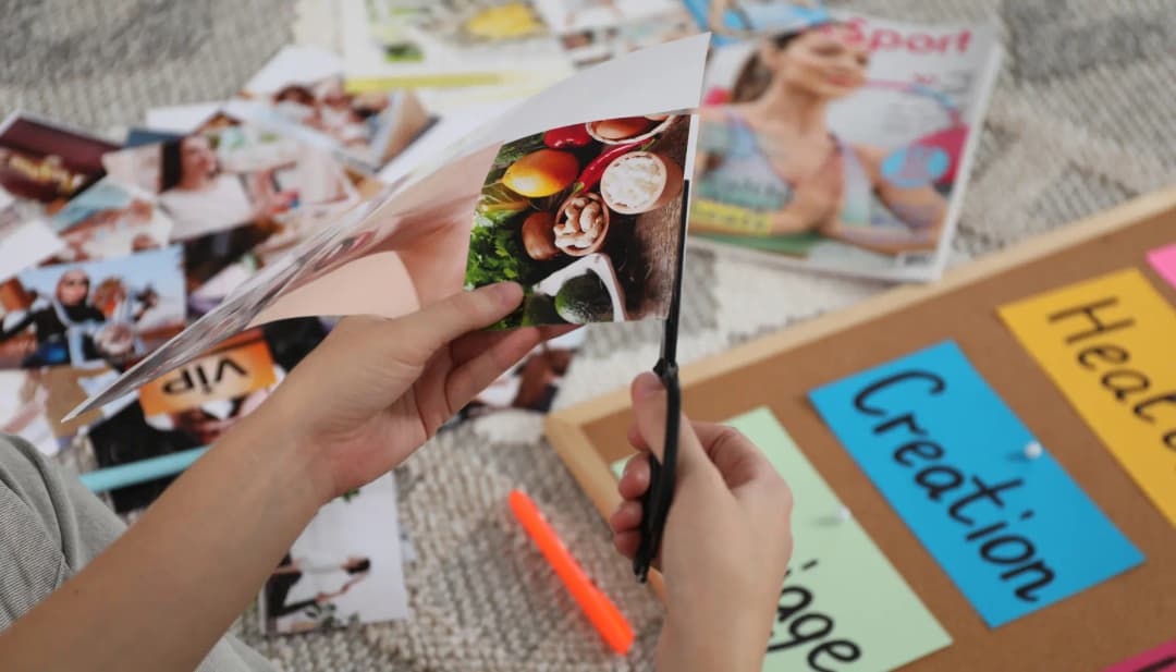 Hände schneiden Bilder aus Zeitschriften für ein Visionboard mit Zetteln