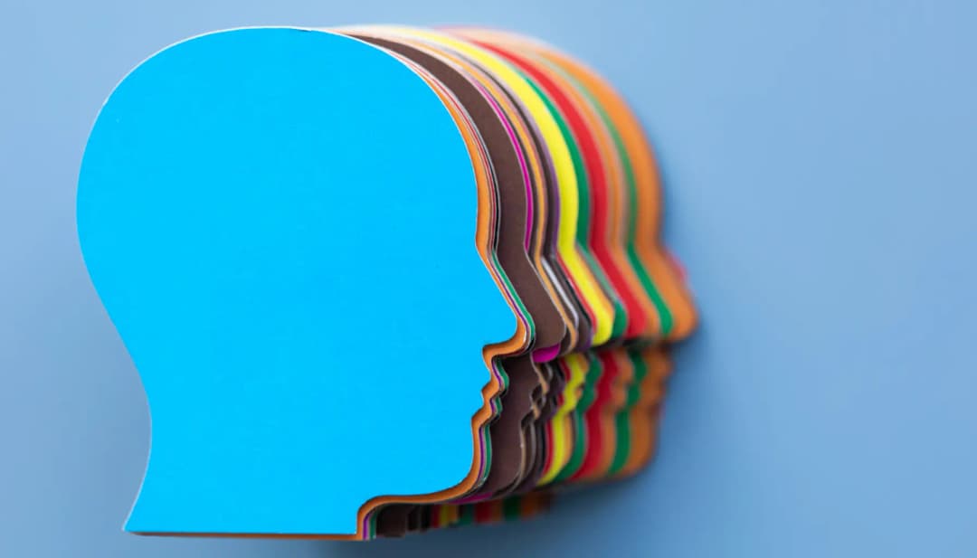 Bunte Kopfprofile aus Papier hintereinander auf blauem Hintergrund