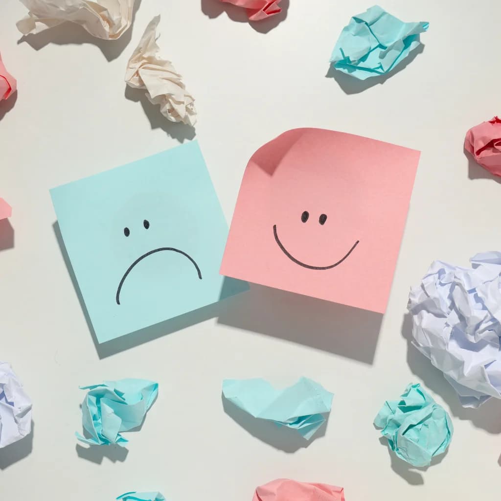 Trauriger und lachender Smiley auf Haftnotizen zwischen zerknülltem Papier