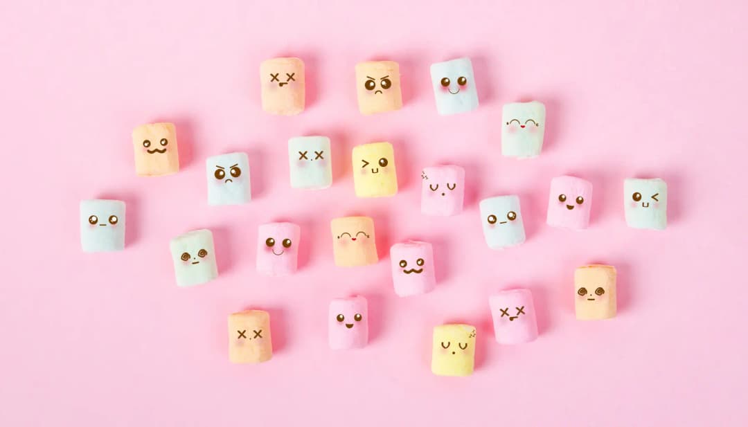 Bunte Marshmallows mit gezeichneten Gesichtern auf rosa Hintergrund