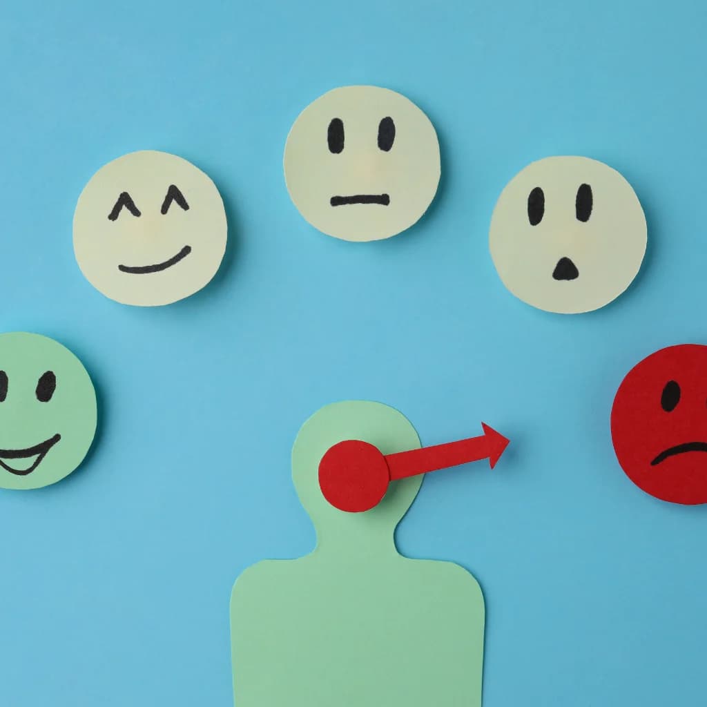 Papierfigur mit Zeiger zwischen Smileys von fröhlich bis traurig