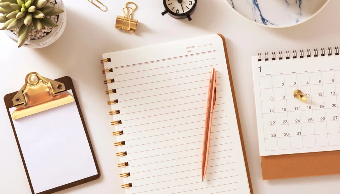 Notizblock, Klemmbrett, Kalender und Stift auf hellem Schreibtisch