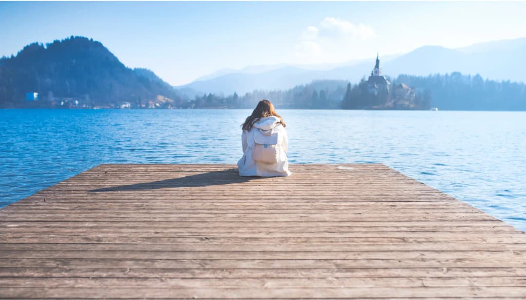 Person sitzt auf einem Steg an einem Bergsee mit kleiner Insel