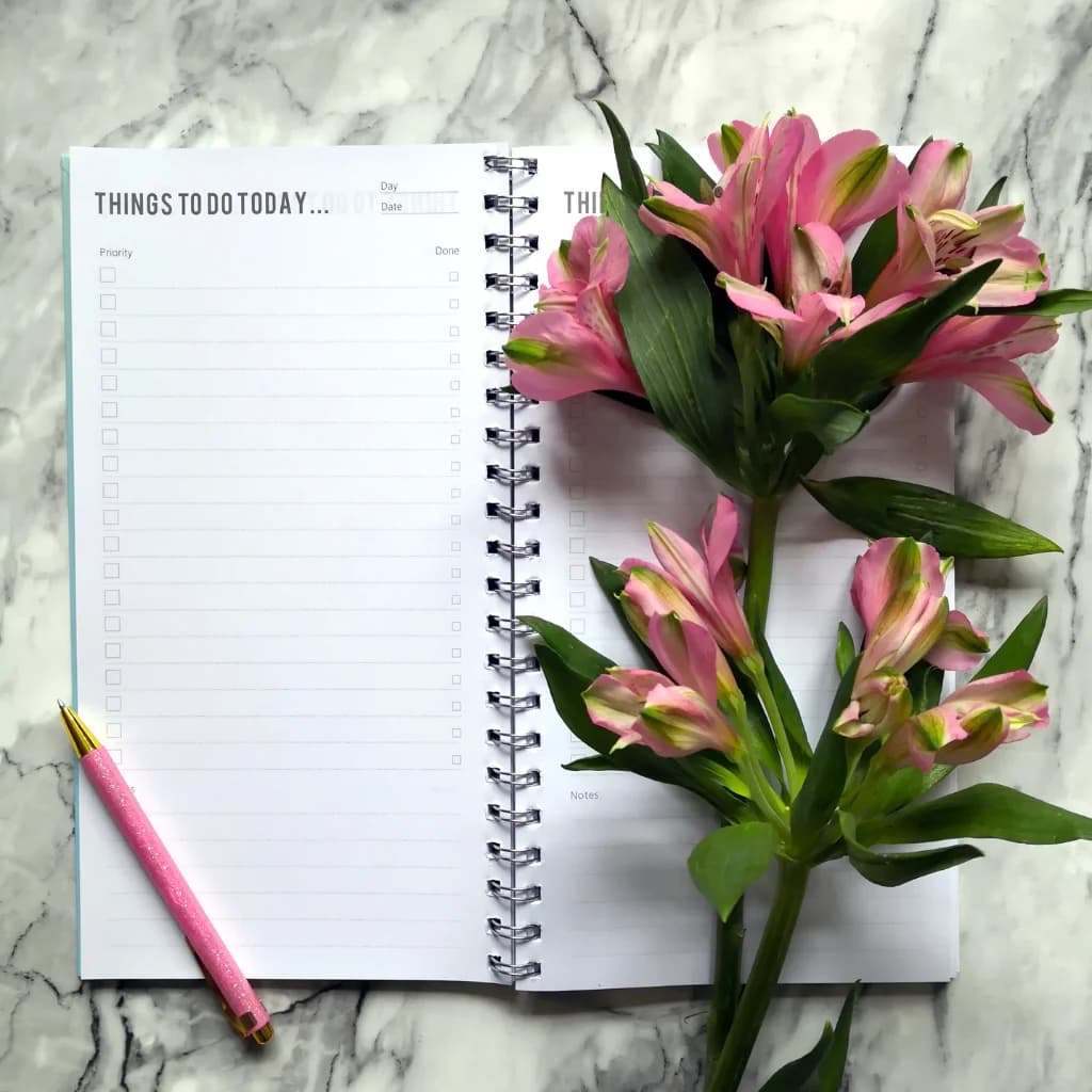 To-do-Liste in einem Spiralblock neben rosa Lilien auf Marmor