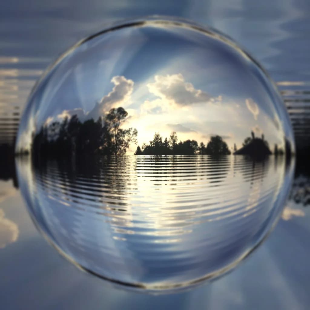 Glaskugel spiegelt einen See mit Bäumen und Wolken
