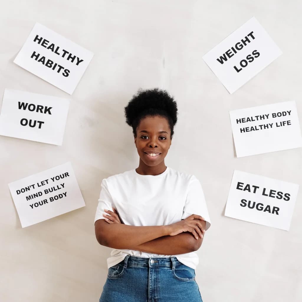 Lächelnde Frau vor einer Wand mit Zetteln wie „Healthy habits“ und „Work out“