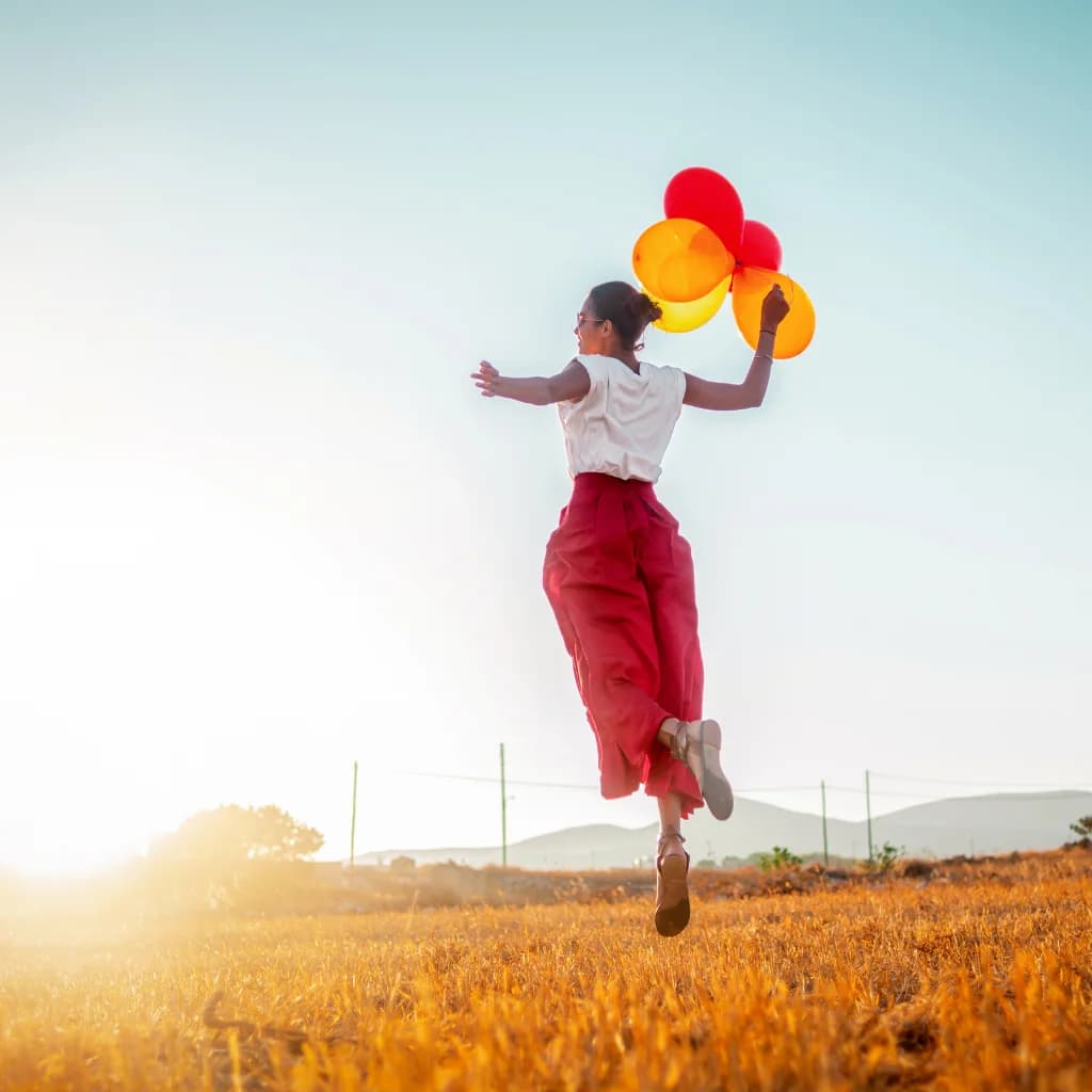 Frau springt mit bunten Luftballons über ein sonniges Feld