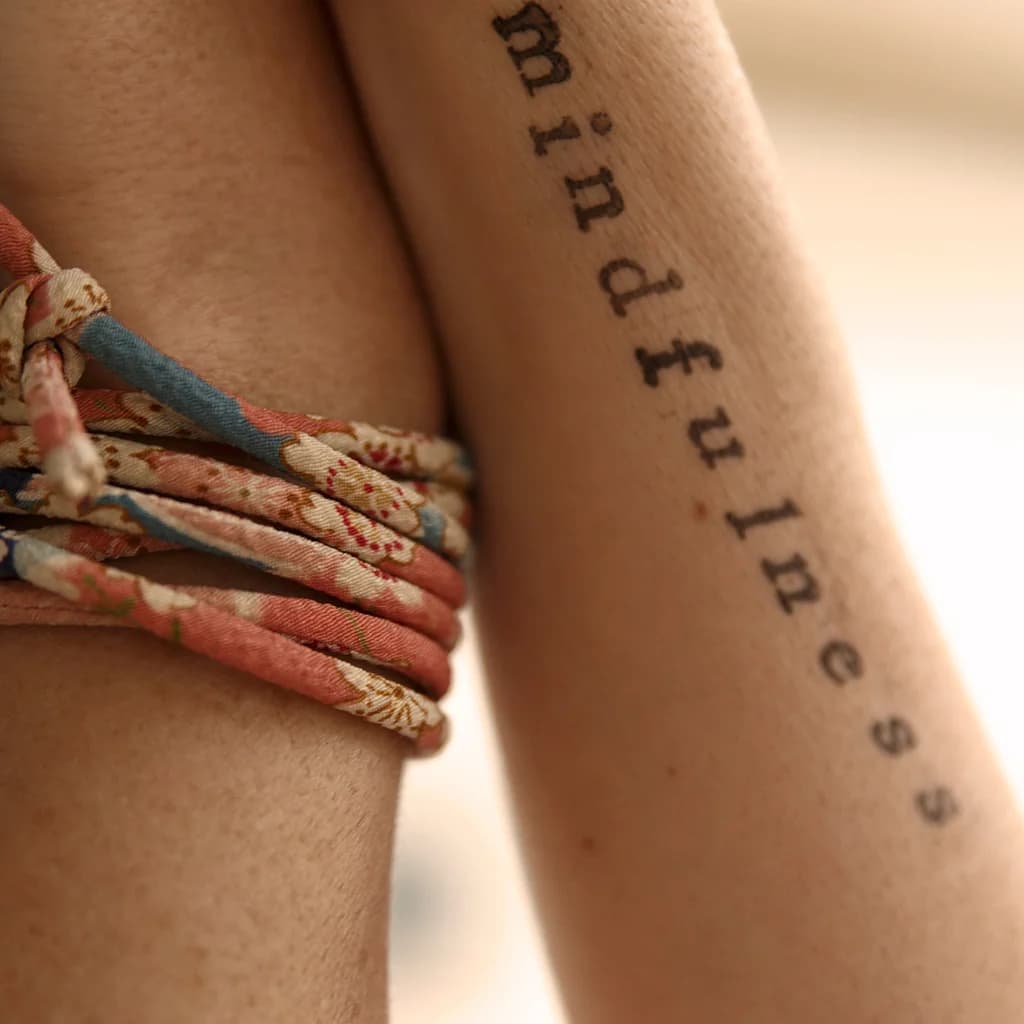 Unterarm mit dem Tattoo „mindfulness“ und bunten Armbändern