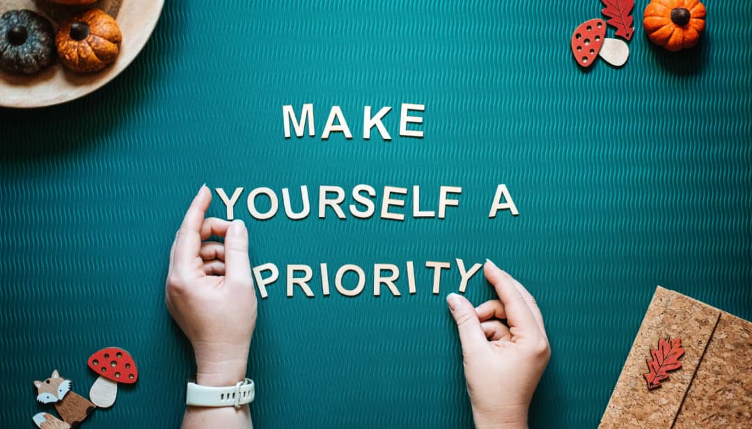 Hände legen auf grünem Filz die Worte „Make yourself a priority“