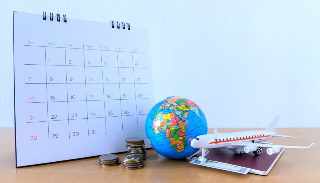 Tischkalender neben Globus, Münzen und einem Spielzeugflugzeug