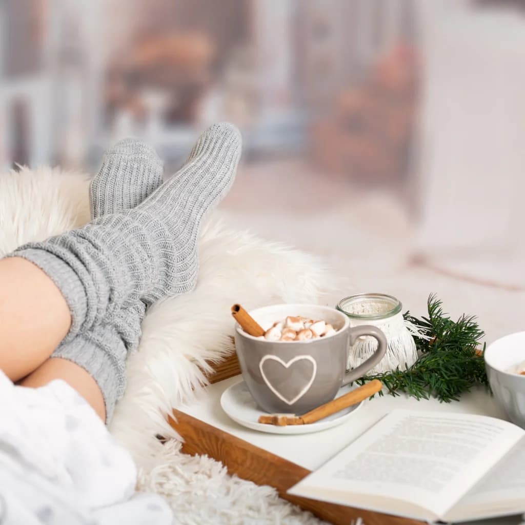 Füße in Wollsocken, Kakao mit Herz, Zimtstangen und ein offenes Buch