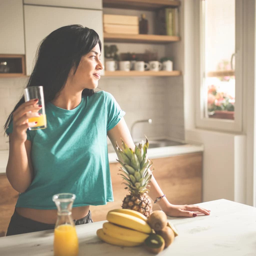 Frau mit Orangensaft in einer hellen Küche, daneben Obst