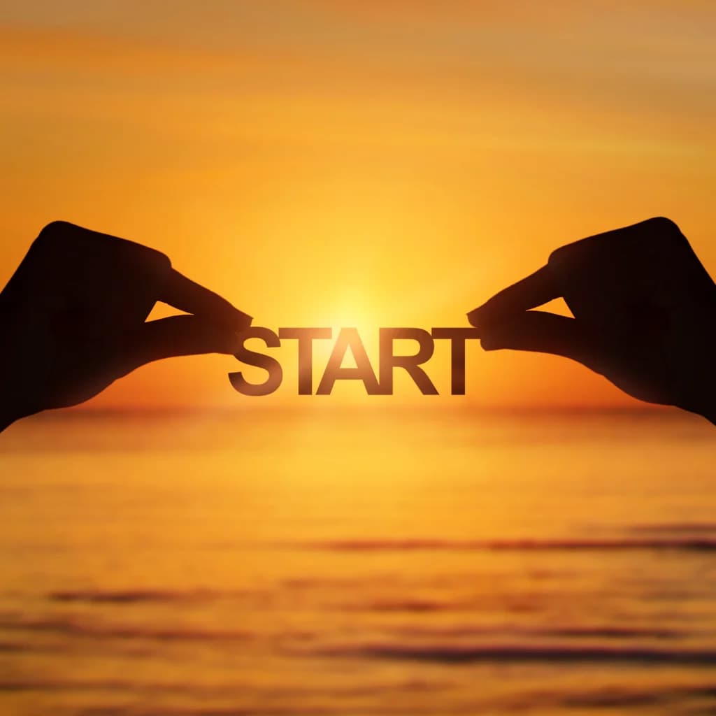 Hände halten im Sonnenuntergang über dem Meer das Wort „Start“