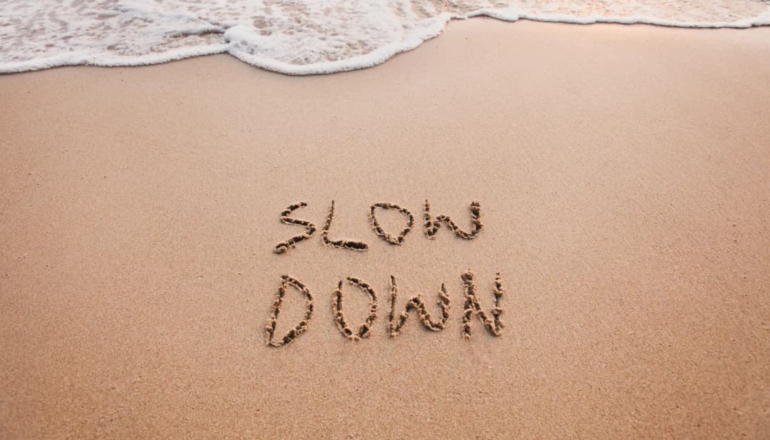 Schriftzug „Slow down“ im Sand am Meeresufer