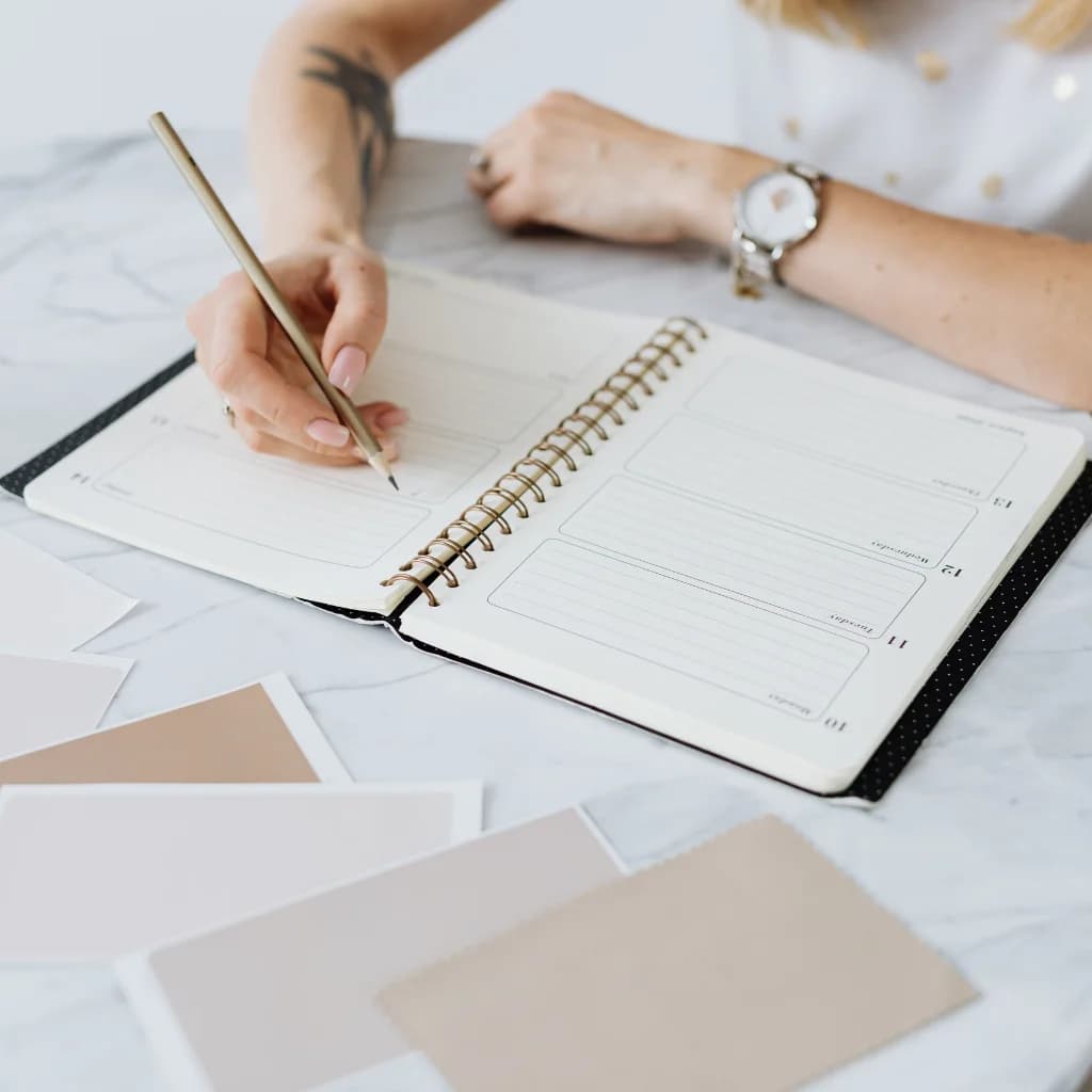 Hand schreibt mit Bleistift in einen Terminkalender