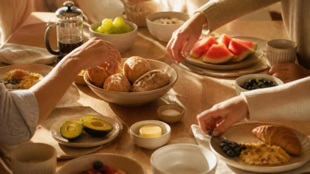 Gedeckter Frühstückstisch am Sonntagmorgen mit Brot, Obst und Kaffee, mehrere Hände greifen zu