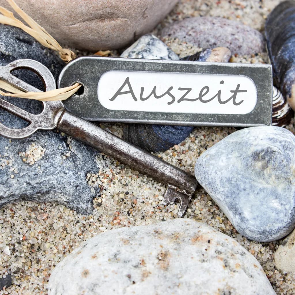 Alter Schlüssel mit Anhänger „Auszeit“ zwischen Steinen im Sand