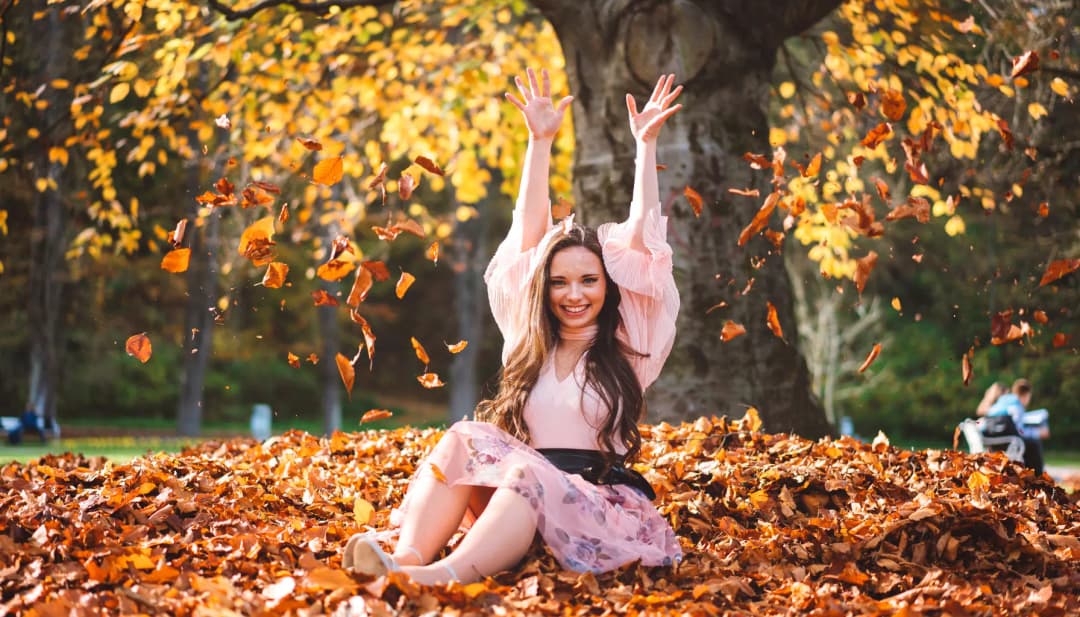 Lachende Frau wirft im Park buntes Herbstlaub in die Luft