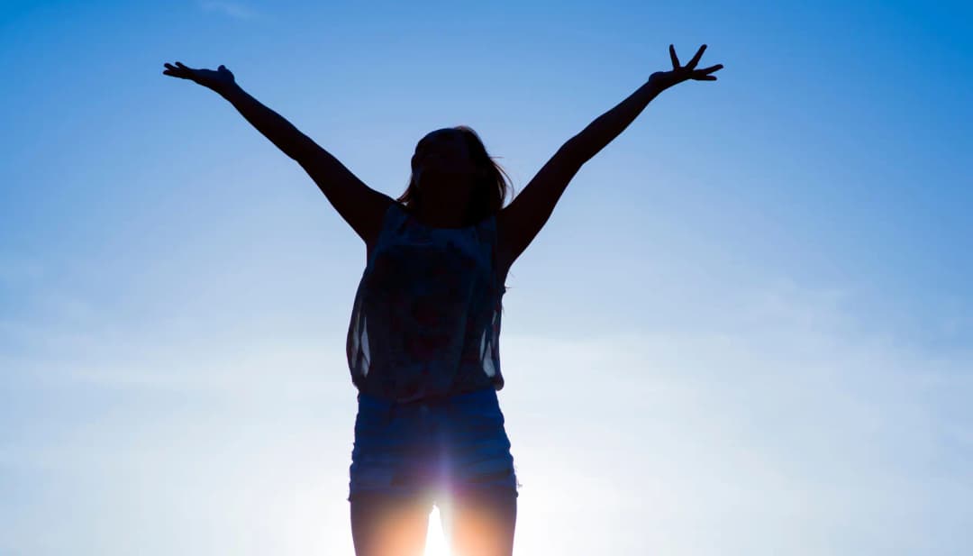 Frau reckt die Arme vor blauem Himmel in die Sonne